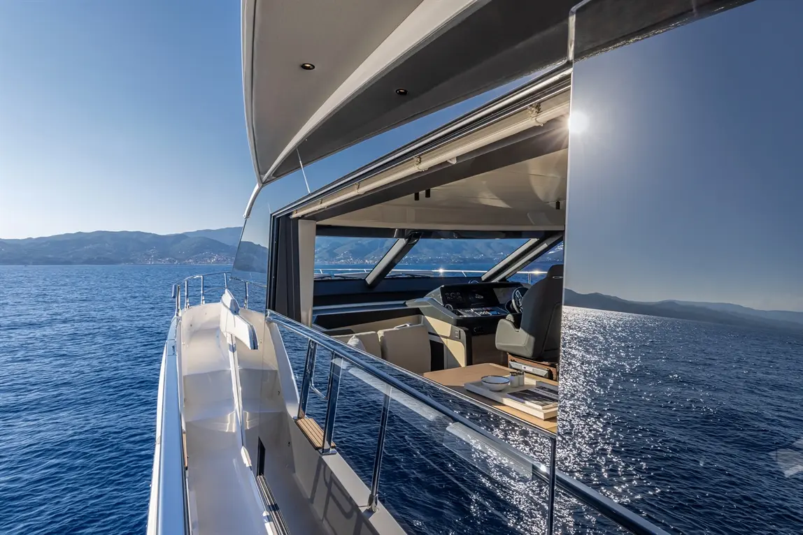 Luxury yacht interior with a modern helm, panoramic ocean views, and mountains in the background on a sunny day.